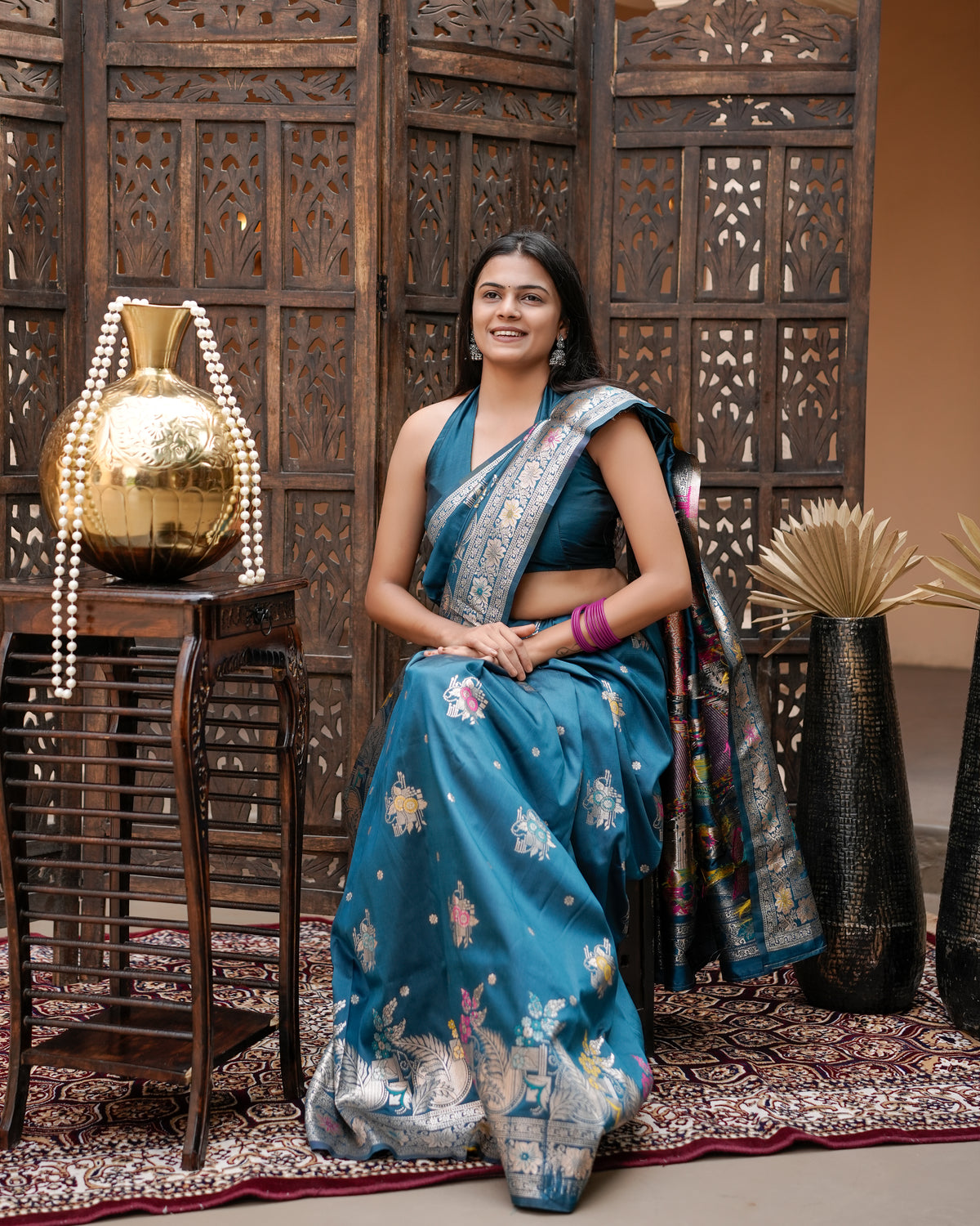 Woman in seated pose wearing deep teal blue Meenakari deer motif zari pallu silk saree — Chandrikas