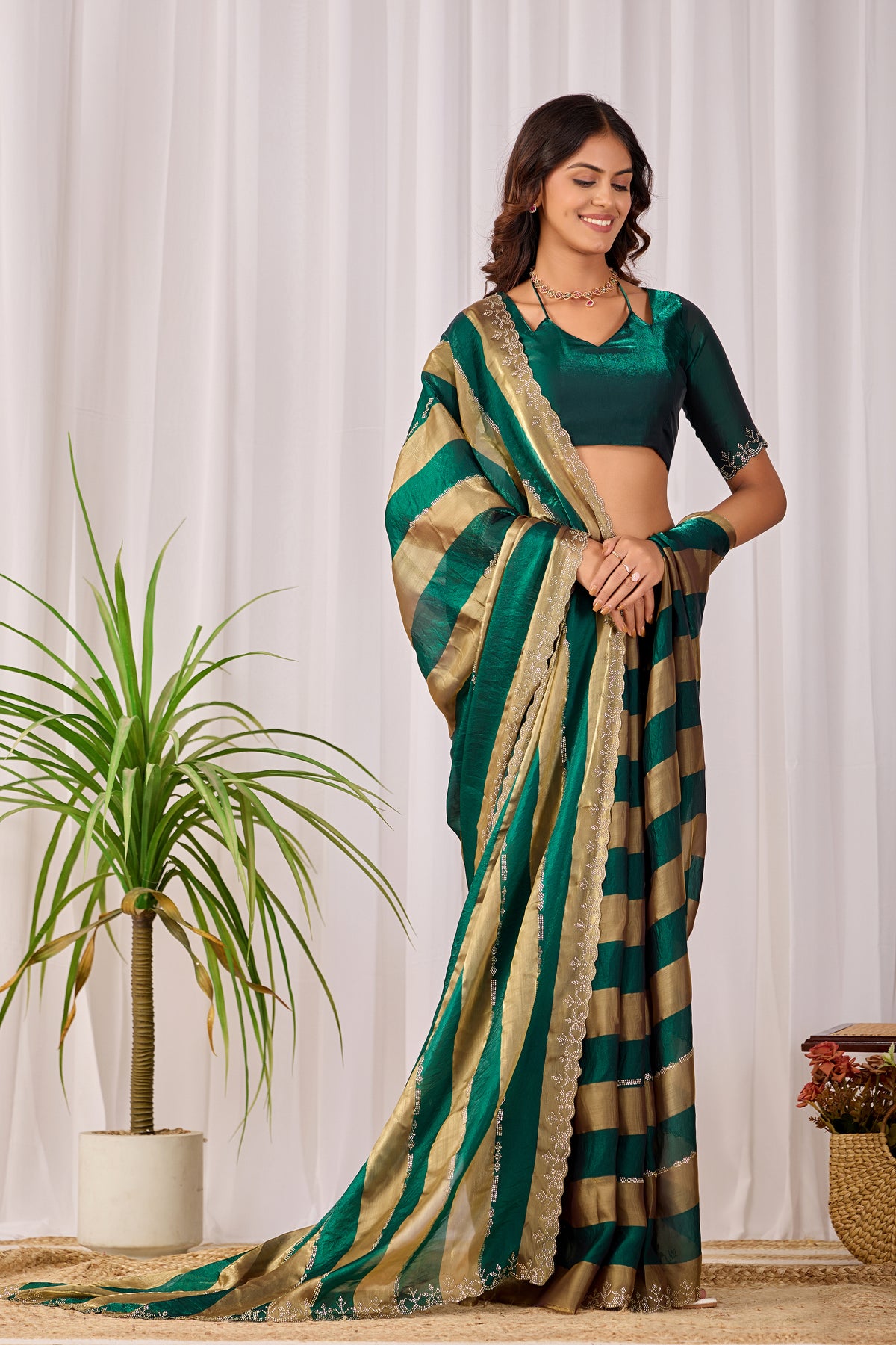 Woman in standing pose wearing emerald green striped satin patta saree with golden pallu — Chandrikas