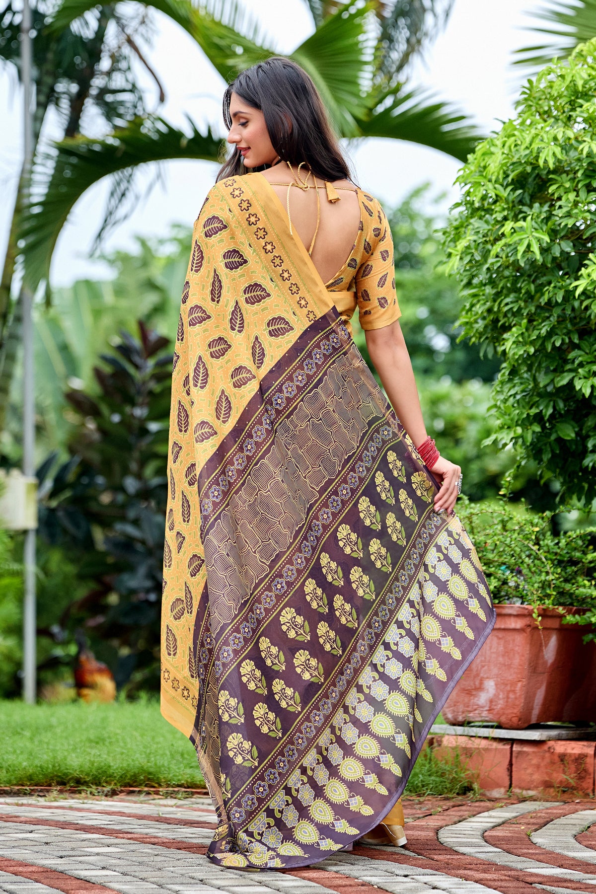 Woman in back pose wearing golden mustard leaf print cotton saree with brown border — Chandrikas