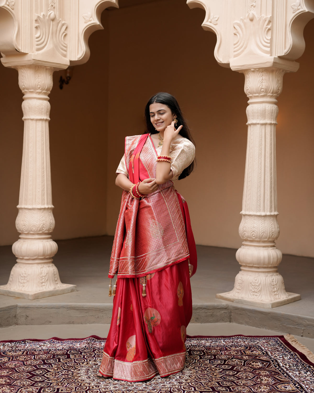 Woman standing near pillar wearing red Banarasi silk Jharkan work diamond jaal saree — Chandrikas