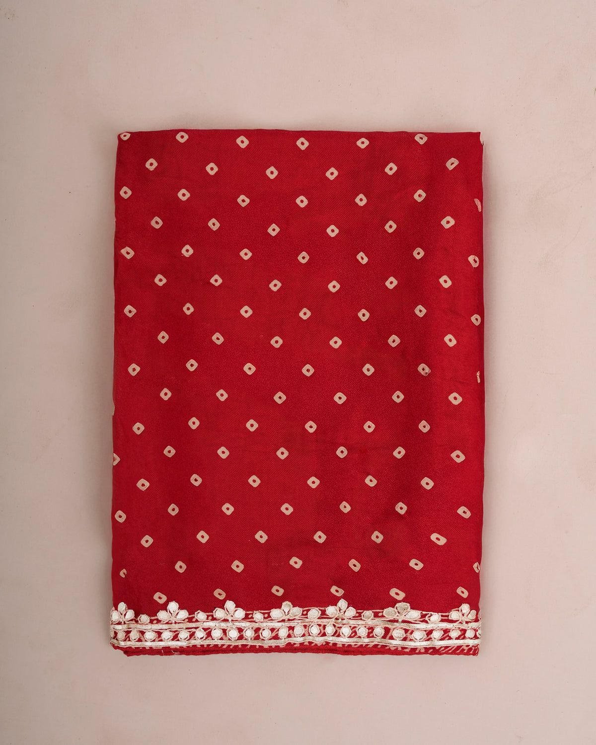 Close-up of folded red Bandhani saree fabric with gota patti lace border — Chandrikas