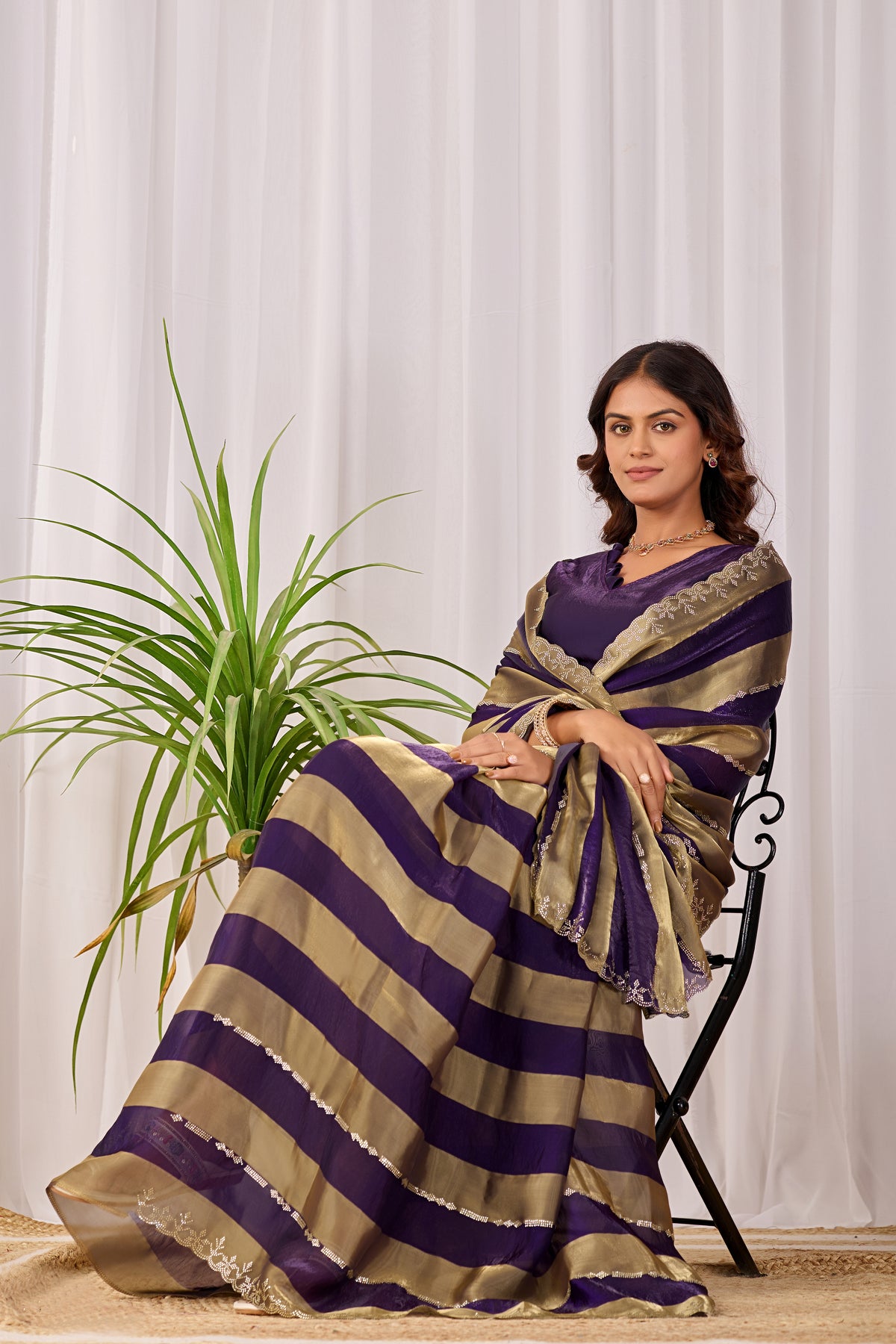 Woman in sitting pose wearing royal purple striped satin patta saree with golden border — Chandrikas