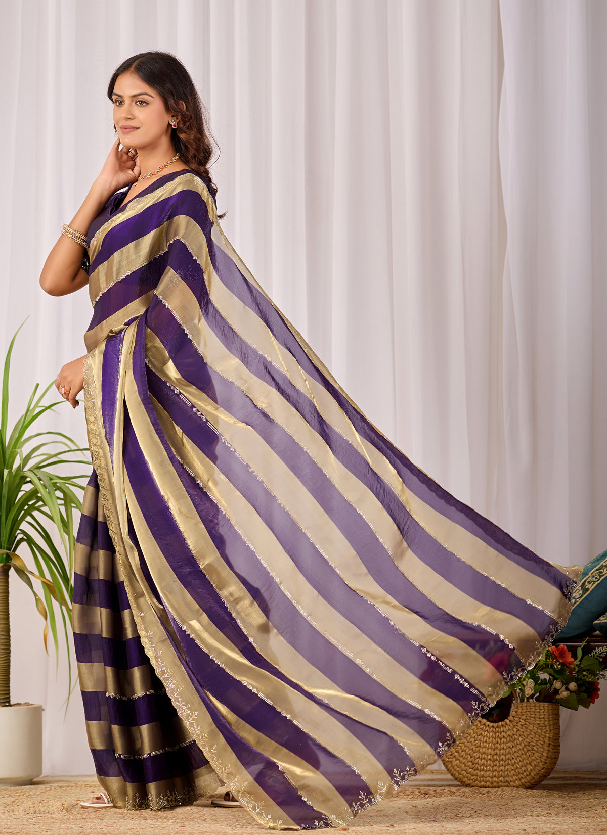 Woman in standing pose wearing royal purple striped satin patta saree with golden pallu — Chandrikas