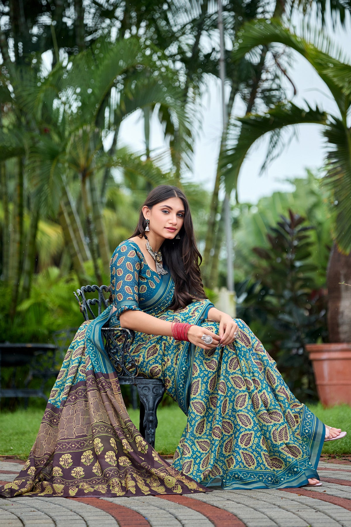 Woman in sitting pose wearing teal blue leaf print cotton saree with brown border — Chandrikas